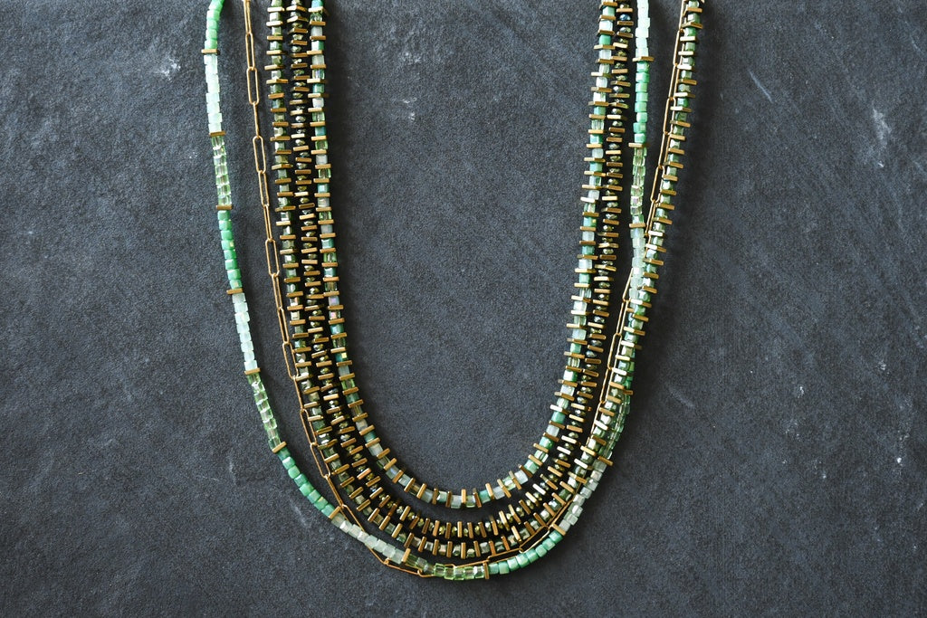 four beaded necklaces in green, gold, and multicolor on a dark gray background