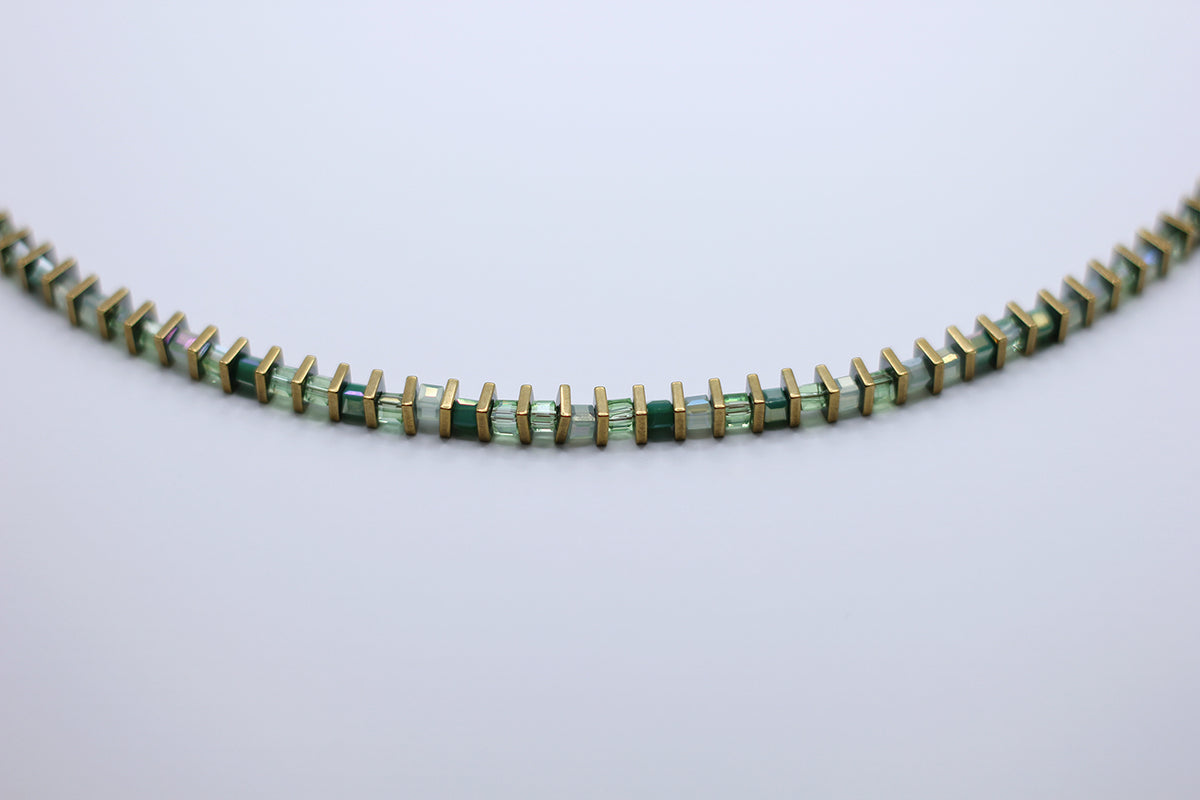 Necklace with green and gold beads on a light gray background